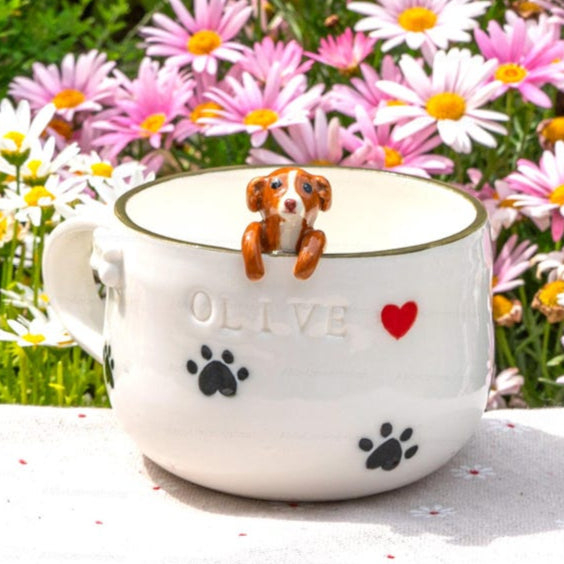 Cup with a small dog figurine on a table surrounded by flowers outdoors