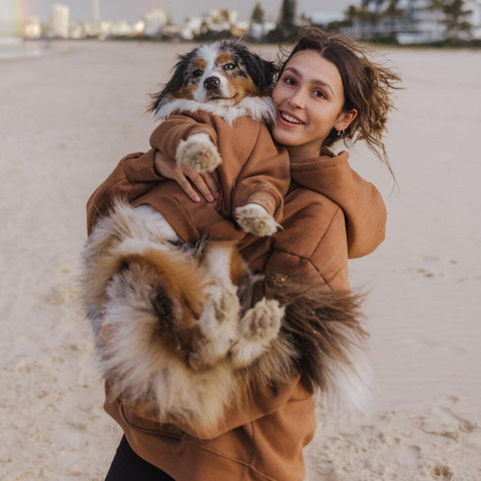 Woman holding a dog on a beach with rainbow in the sky
